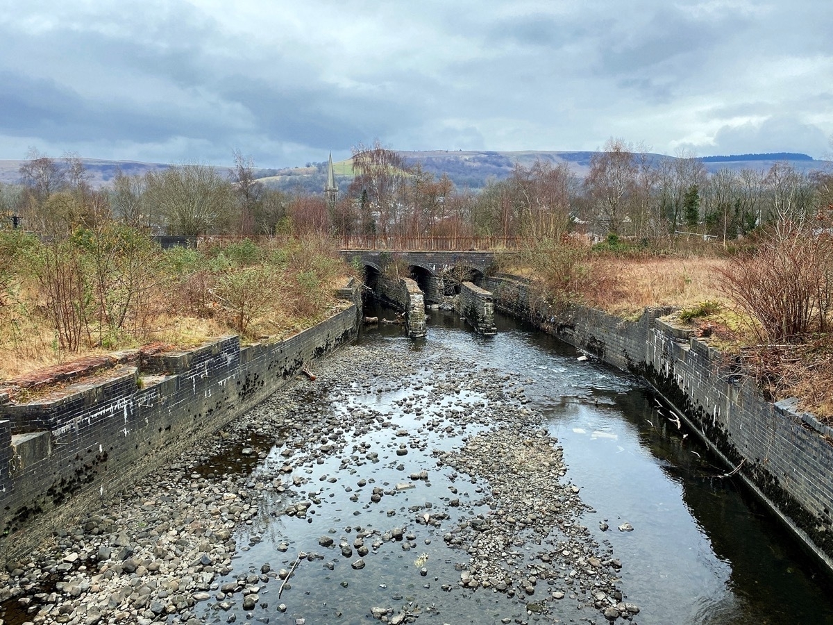 Stone filled river flowing under a bridge, horizon of hills and grey skies in the background