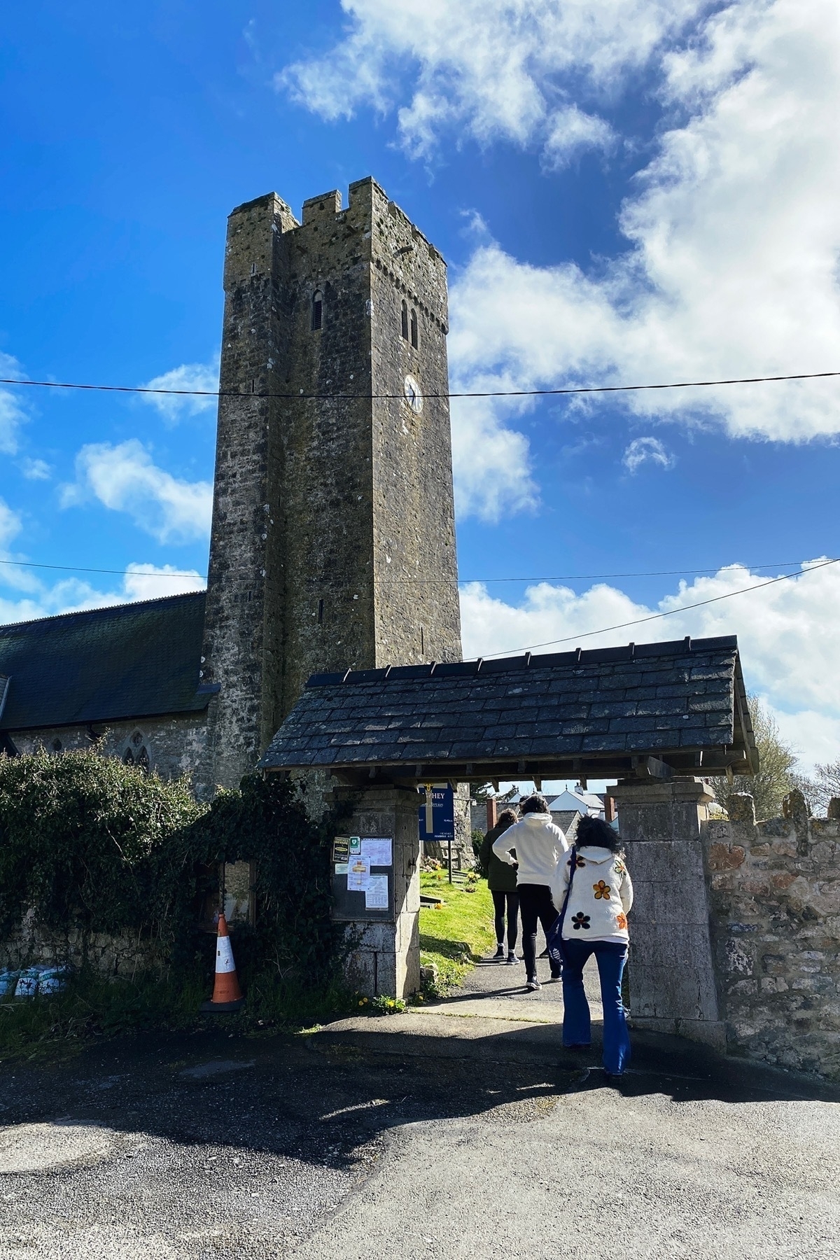 Three people walking through church gate towards a stone church tower