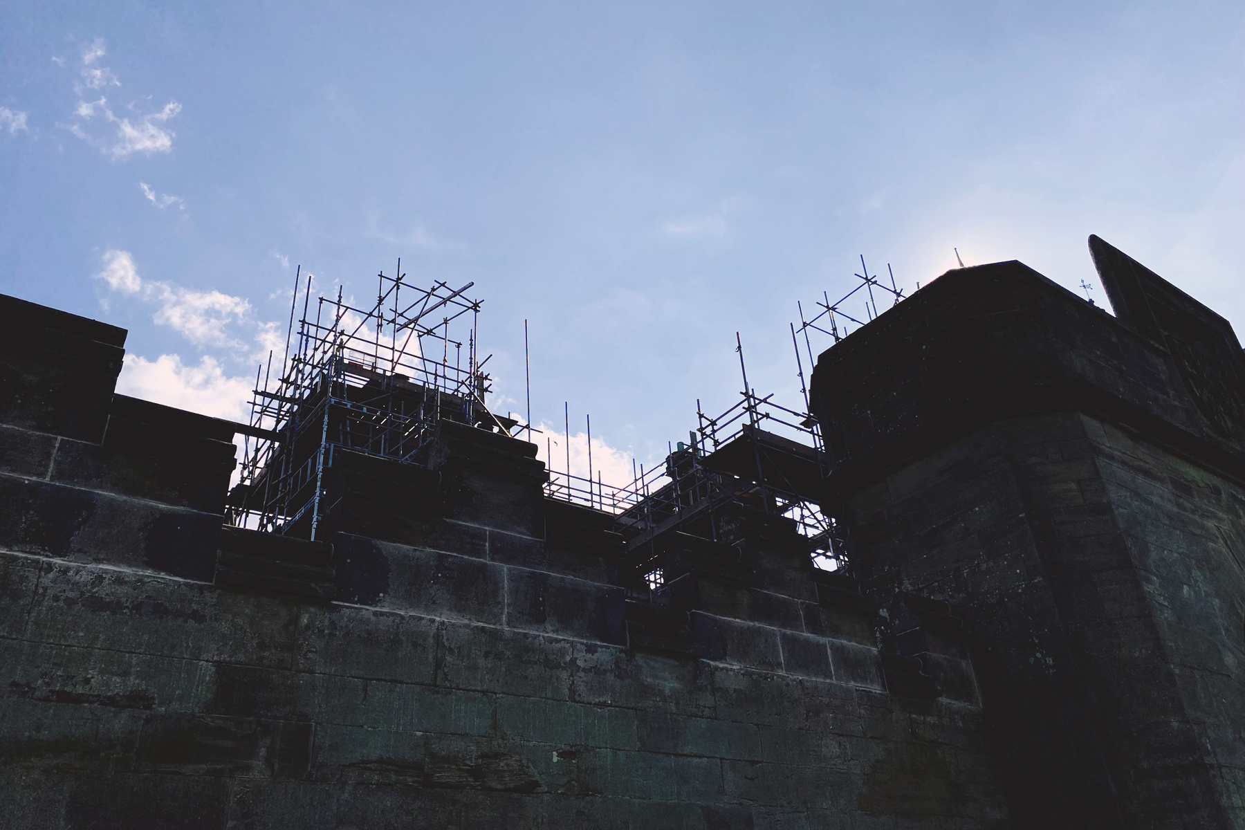 Stone walls and scaffolding silhouetted against a blue sky