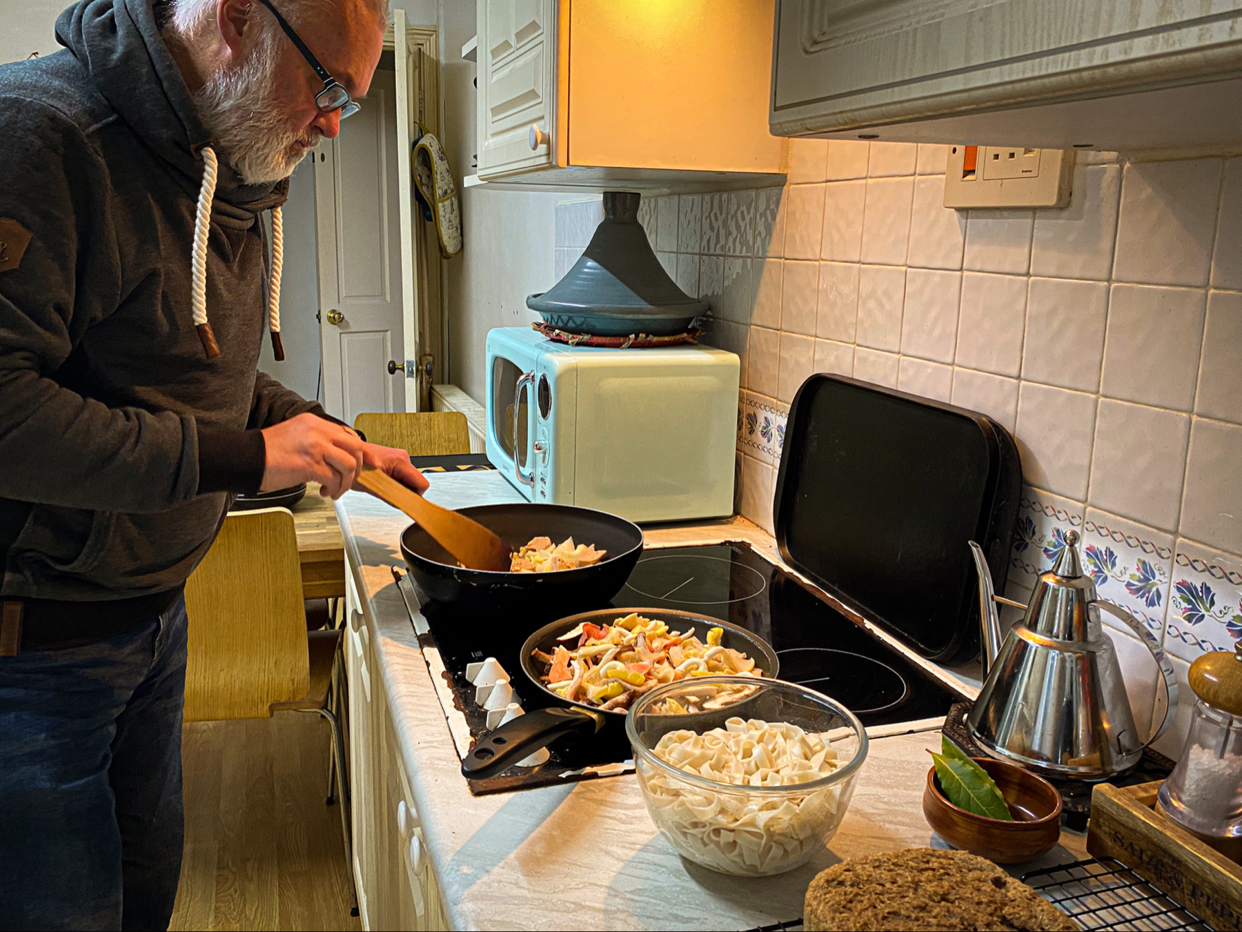 Kitchen scene of a bearded man stir-frying food in a wok