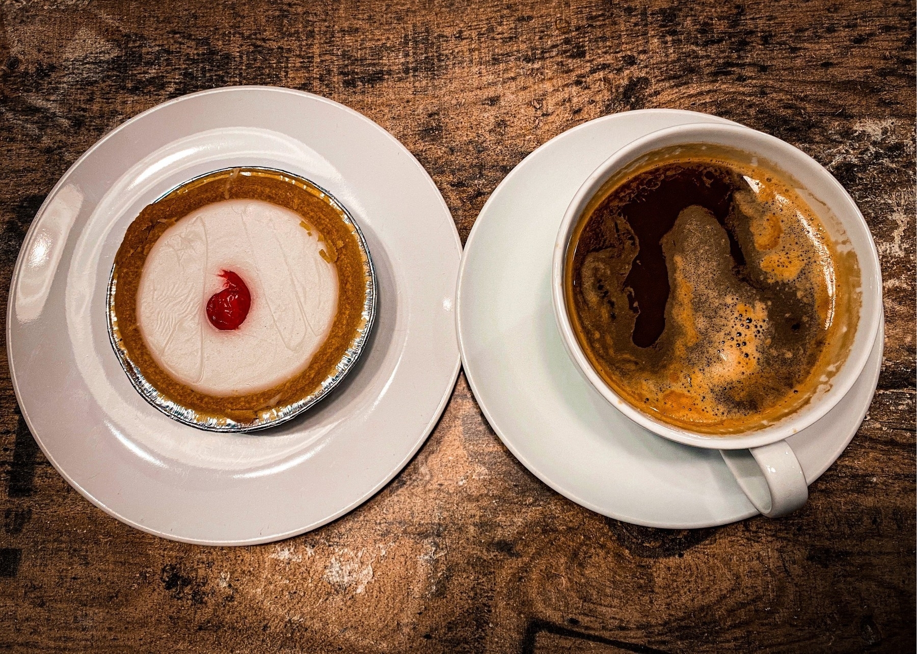 Top down view of an Americano and a cherry bakewell on a wooden table