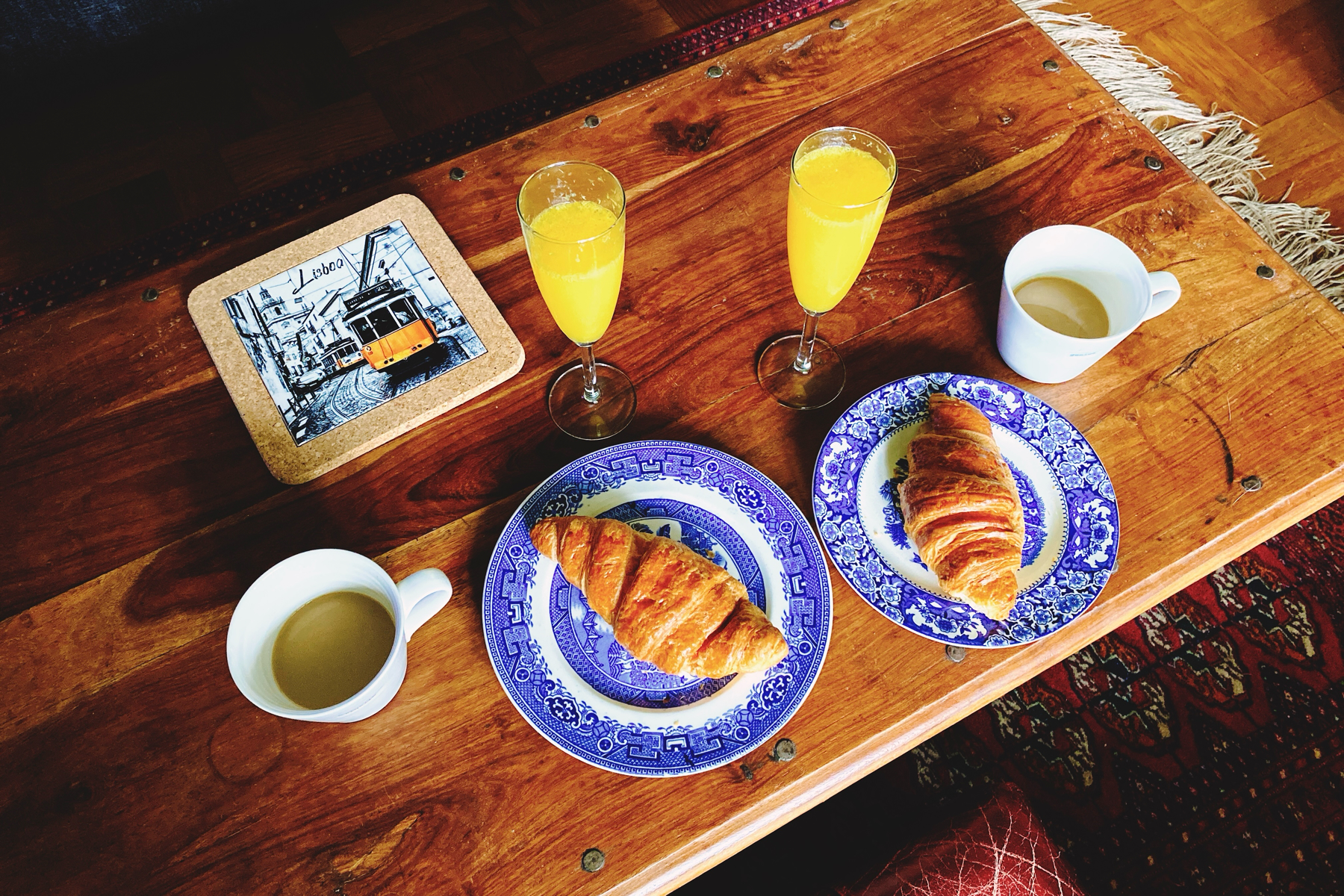 Wooden coffee table set with 2 cups of coffee, 2 plates with croissants and 2 mimosas 