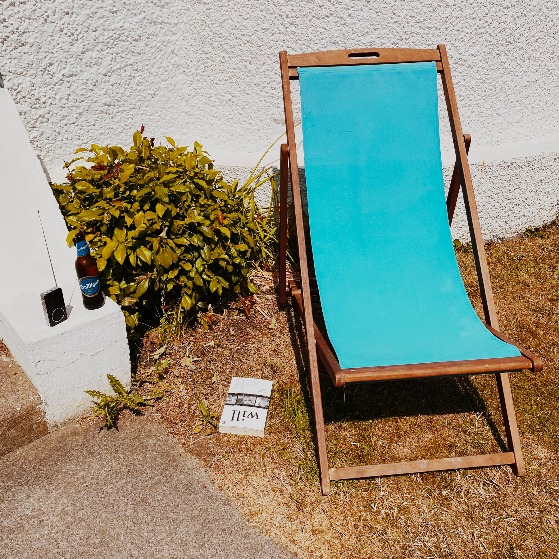 Bright blue deckchair on grass next to a book, bottle of beer and small radio