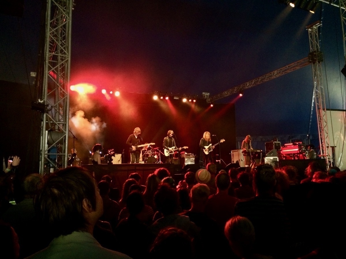 Rock band on a stage in a festival tent under red lighting, audience in foreground