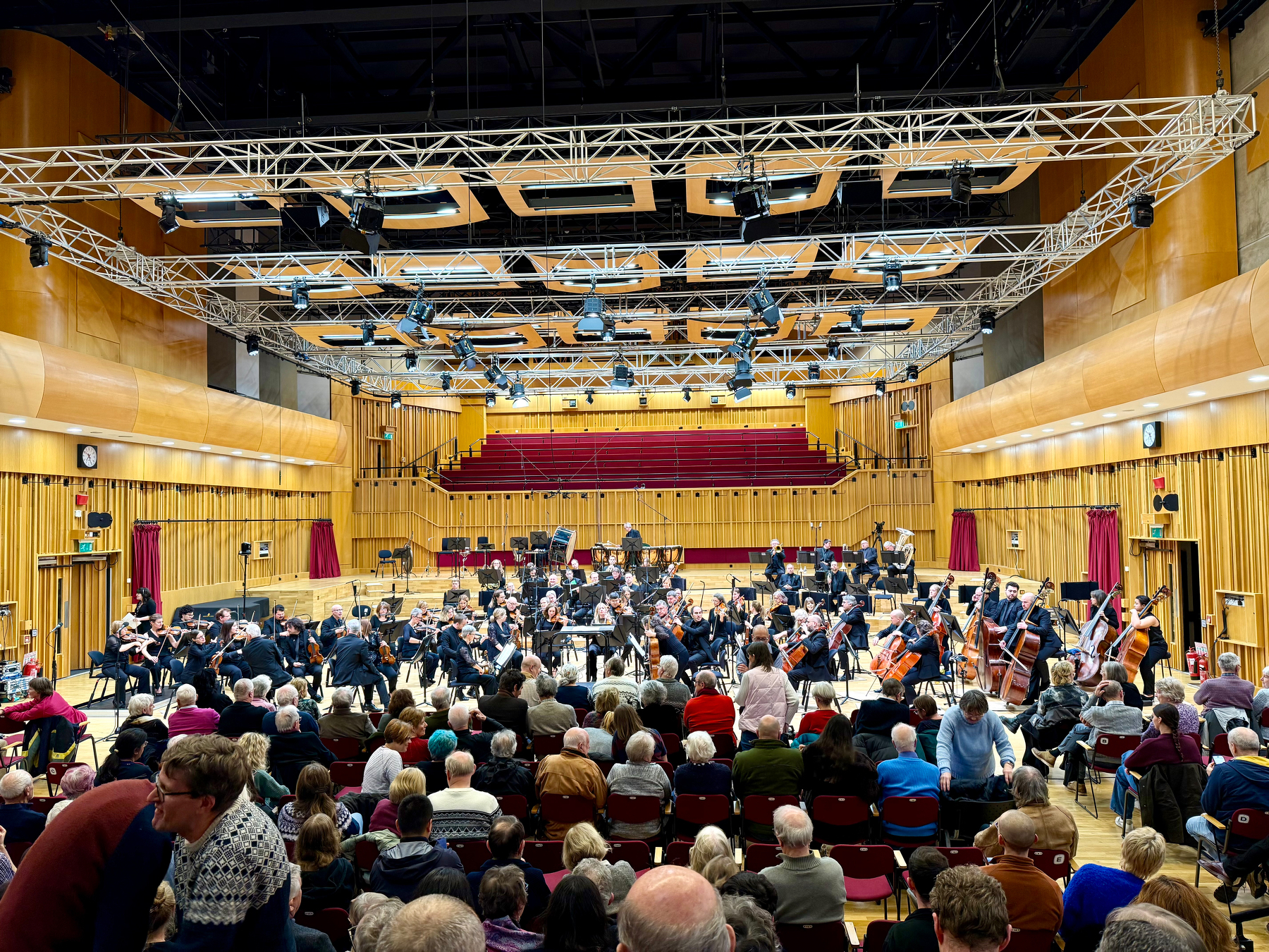 Auto-generated description: A symphony orchestra performs on stage in a concert hall filled with an audience.