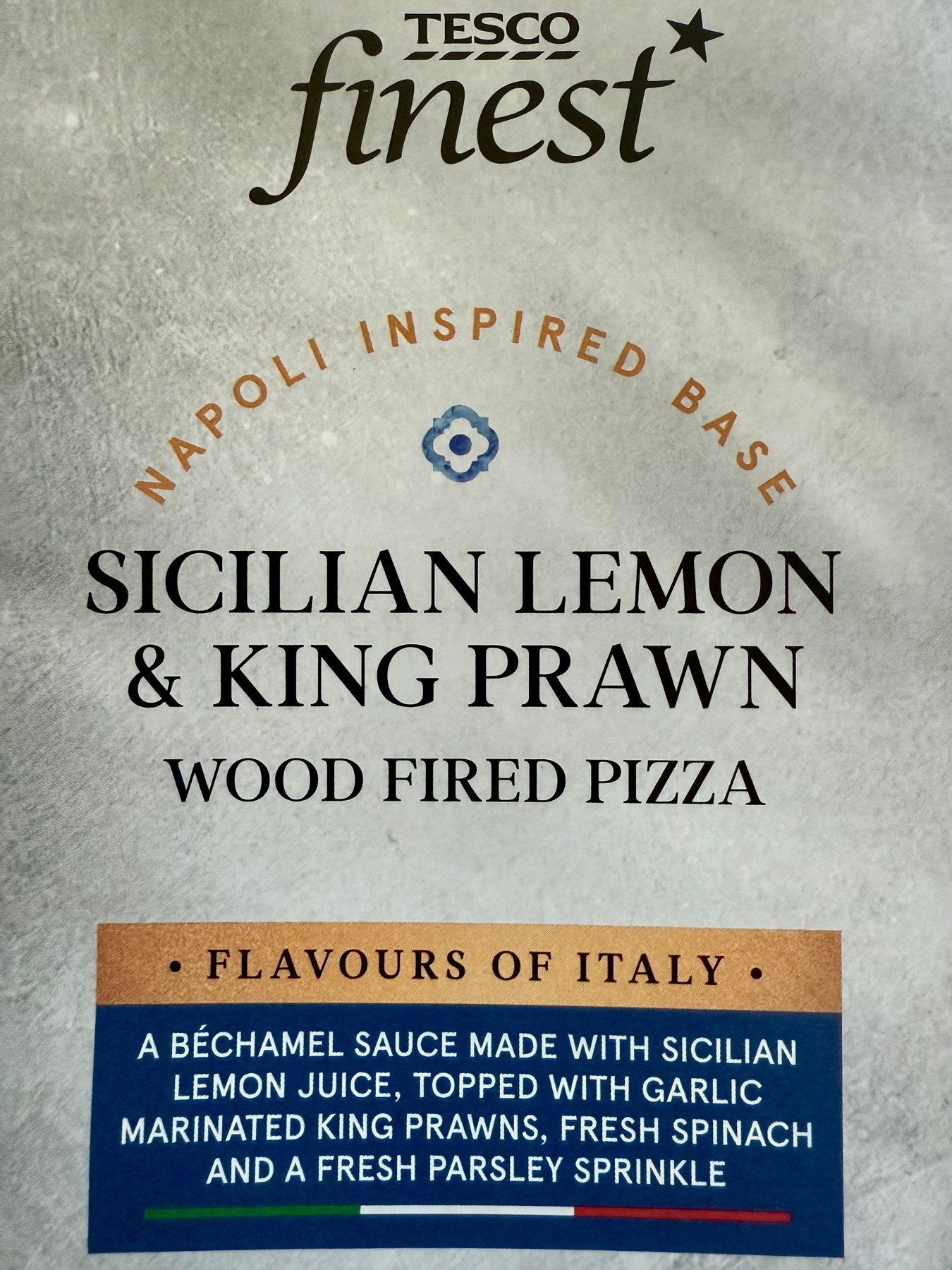 Auto-generated description: A Tesco Finest Sicilian Lemon & King Prawn wood-fired pizza package highlights a Napoli-inspired base with a béchamel sauce, lemon juice, garlic-marinated king prawns, fresh spinach, and parsley.