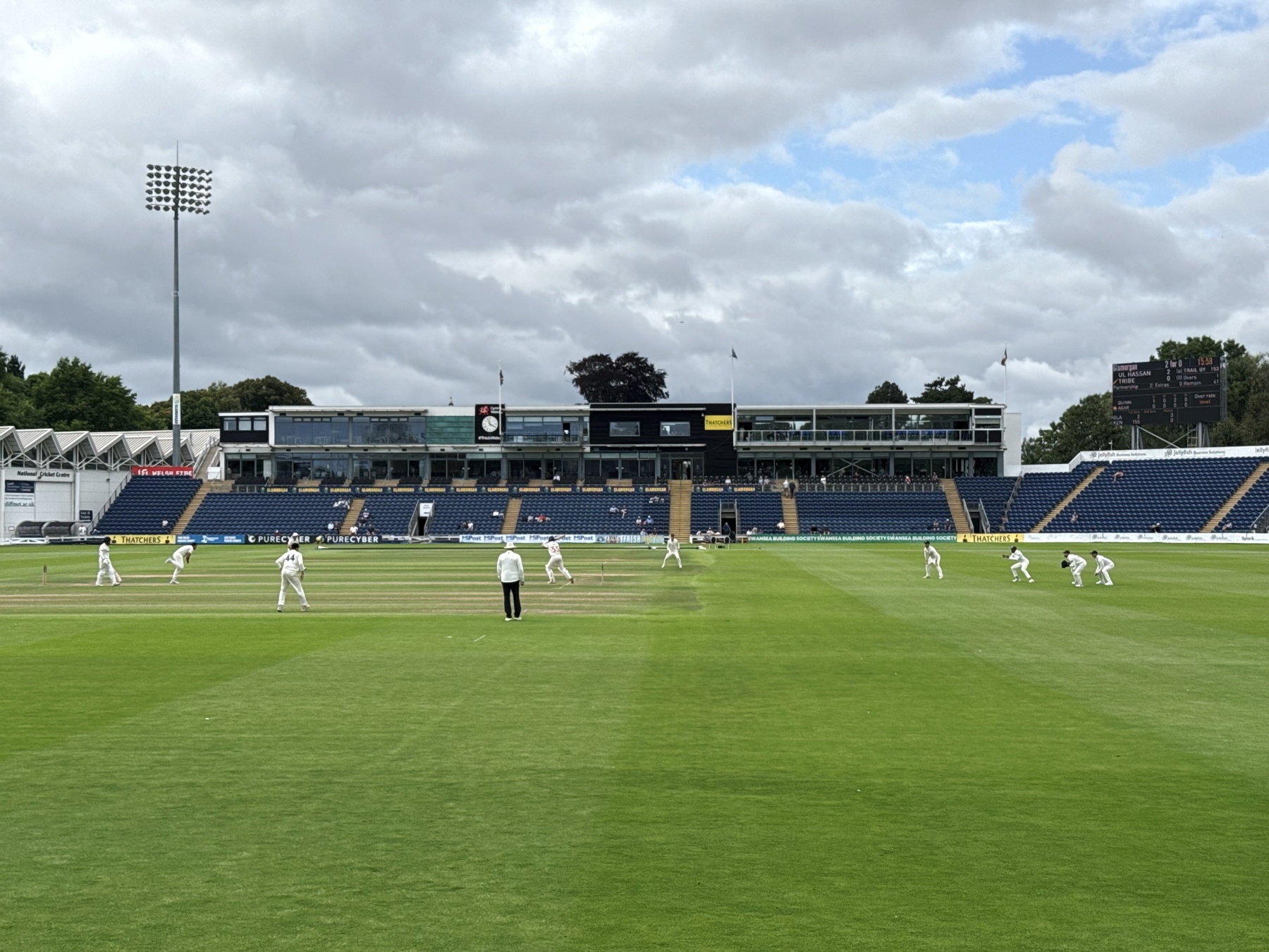Auto-generated description: A cricket match is being played in a stadium with players positioned around the field and a large seating area in the background.