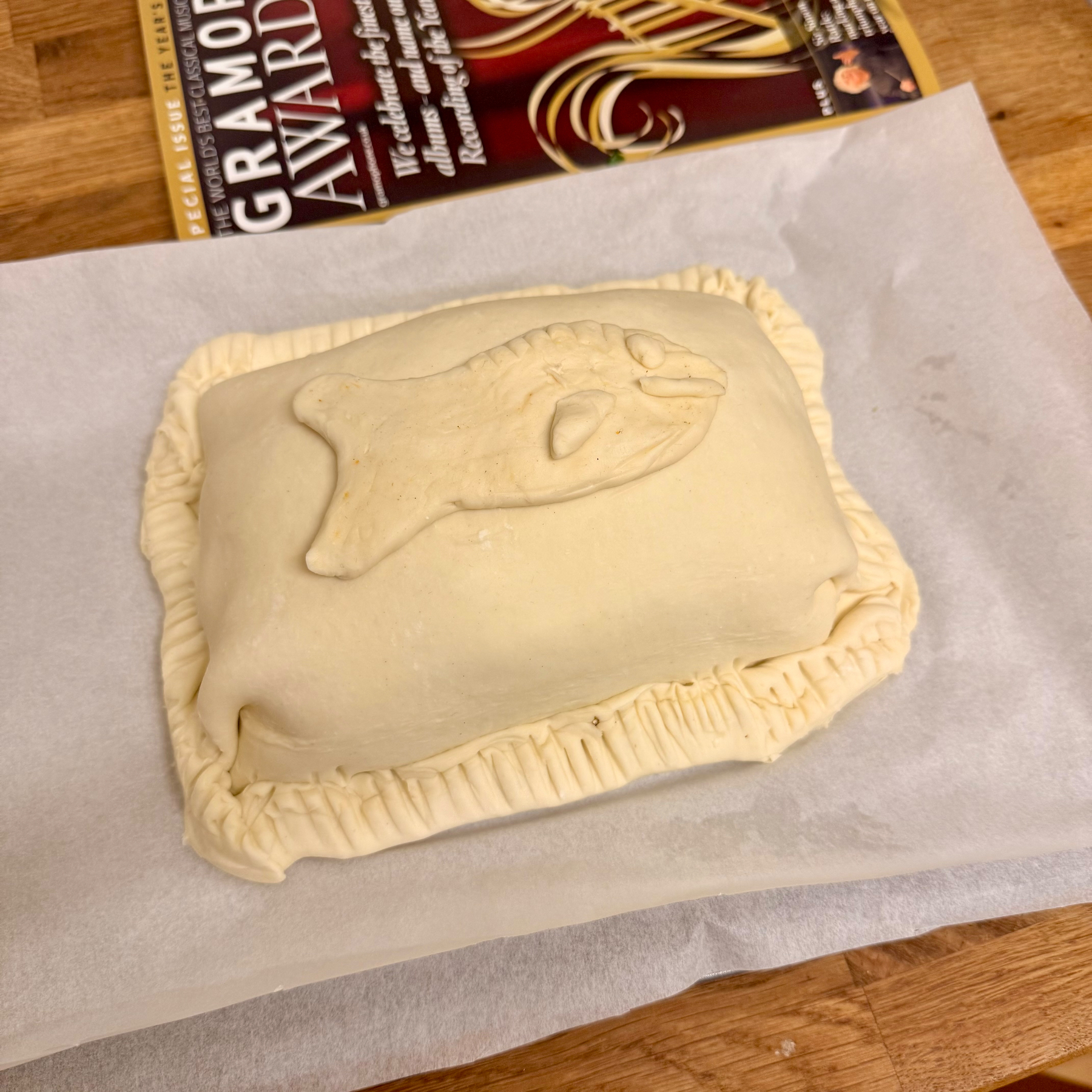 Auto-generated description: A rectangular pastry with crimped edges and a fish-shaped design on top rests on parchment paper.