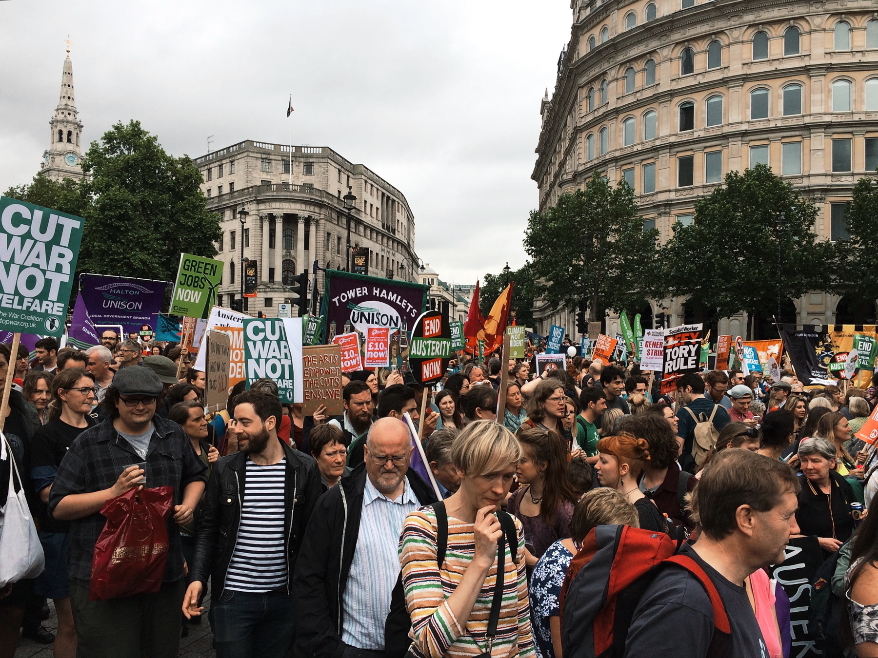 Auto-generated description: A large crowd of people is participating in a protest with various signs and banners in an urban setting.