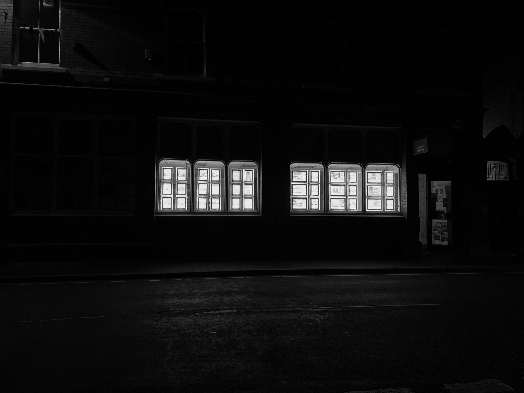 Auto-generated description: Brightly lit windows illuminate a dark street at night.