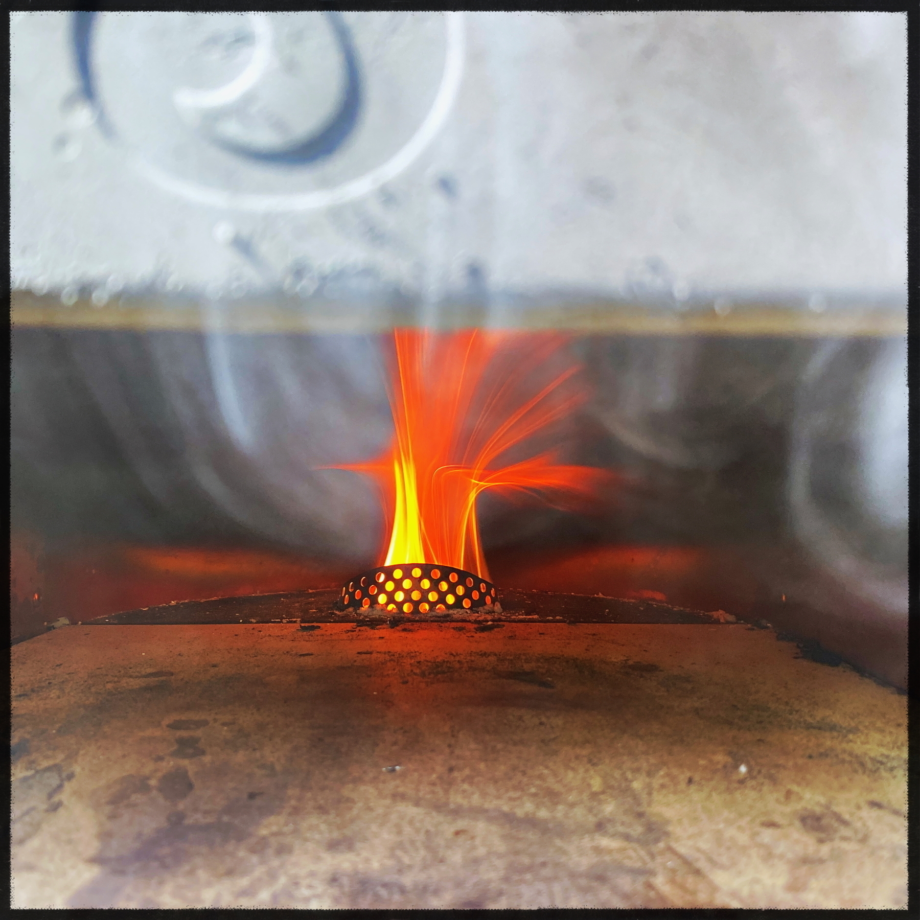 Auto-generated description: A lit gas burner inside a metallic oven emits flames and subtle smoke.