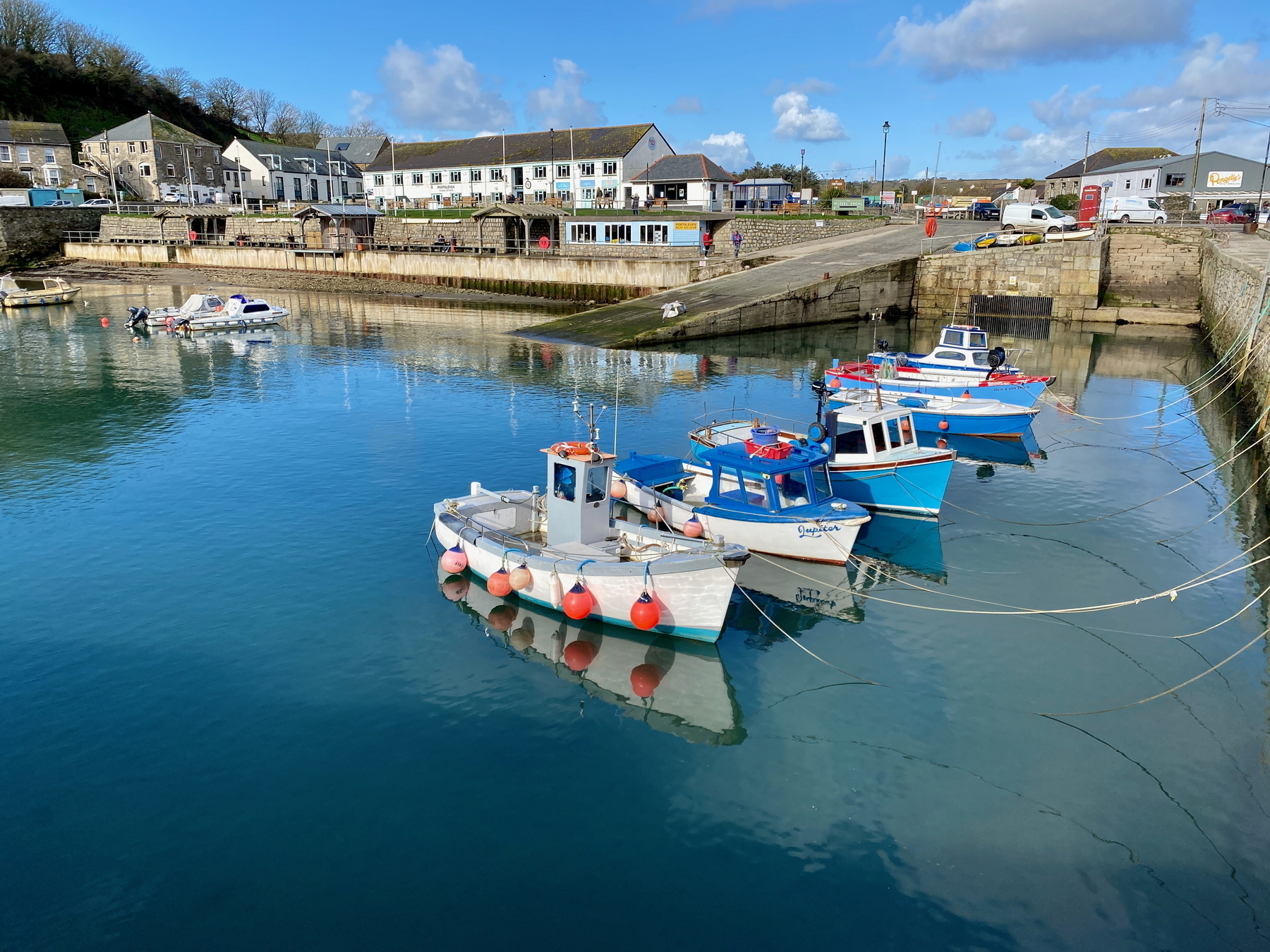 Auto-generated description: Colorful boats are tied up in a calm harbor surrounded by buildings and a clear blue sky.