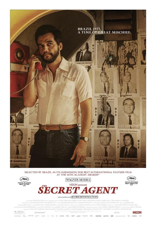 Auto-generated description: A man stands by a rotary phone in a room adorned with various posters, set in Brazil in 1977, as depicted in the movie poster for The Secret Agent.
