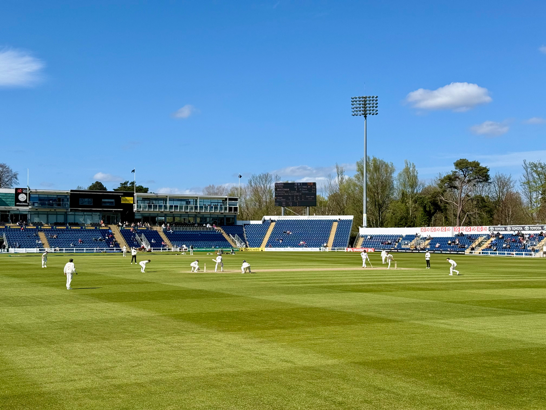 Auto-generated description: A cricket match is taking place in a stadium with players on the field and spectators in the stands under a clear blue sky.